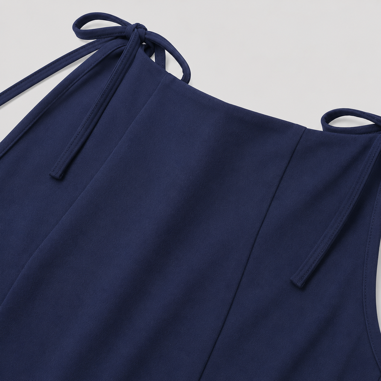 Sleeveless peplum top with boat neckline, shoulder tie accents, sculpted seams, and tailored waist for an elegant structured silhouette